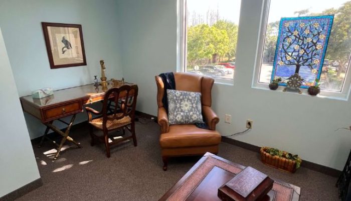 This is an image of a therapist office in Stuart, Fl with a brown desk, chair, and, coffee table with various art pieces.